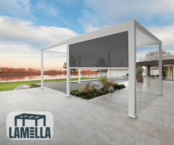 Auf einer geräumigen gefliesten Terrasse steht eine moderne Pergola mit einem manuell einziehbaren Lamellendach und Seitenmarkise. In der Nähe erstrecken sich ein gepflegter Garten und eine ausgedehnte Rasenfläche zu einem ruhigen See hin, alles unter einem strahlenden Himmel. Das Logo lautet „Lamella“.