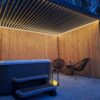 In der Abenddämmerung lädt der Außenbereich mit einem modernen Whirlpool und Treppen unter einer Pergola mit LED-Beleuchtung und Lamellendach zum Verweilen ein. Zwei dunkle Stühle, ein kleiner Tisch mit Getränken und eine Laterne mit Kerzen stehen auf dem Kiesboden, während Bäume eine ruhige Kulisse bieten.