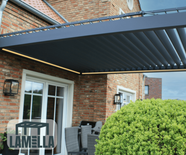 Eine moderne Terrasse präsentiert eine maßgefertigte Pergola „Lamellendach nach Maß“ in Blau, die nahtlos an ein Backsteinhaus angebaut ist und Schatten über den Gartenmöbeln spendet. Ein ordentlich geschnittener Strauch schmückt den Vordergrund. In der unteren linken Ecke wird das Wort LAMELLA zusammen mit einem stilisierten Tischsymbol angezeigt.