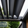 Nahaufnahme einer modernen Pergola im Freien mit individuell gestalteten, verstellbaren Lamellendachpaneelen, teilweise geöffnet. Im Hintergrund ist üppiges grünes Laub zu sehen, das die natürliche Schönheit der Umgebung unterstreicht. Eine Glaswand verleiht eine elegante Note. In der unteren linken Ecke ist ein Logo mit dem Namen „Lamellendach nach Maß (Preis auf Anfrage)“ zu sehen.