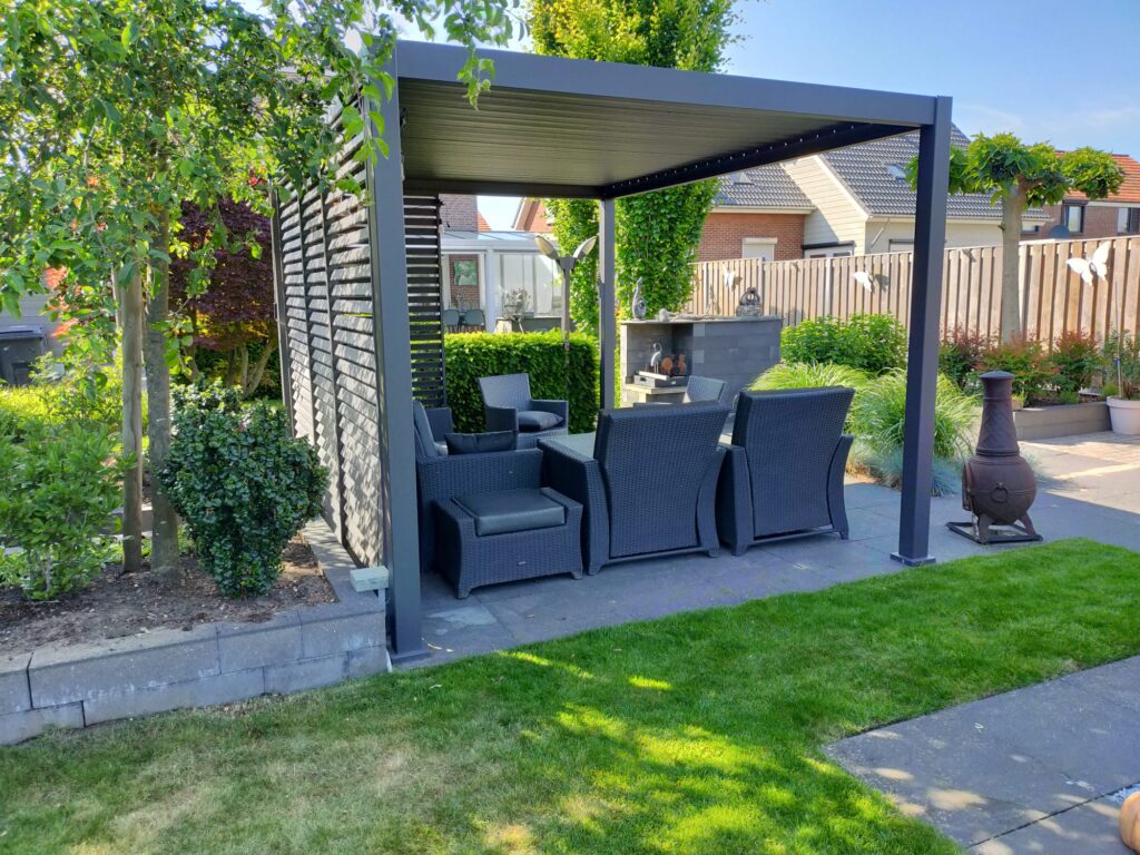 Eine Terrasse im Hinterhof verfügt über eine moderne Pergola mit schwarzen Gartenmöbeln aus Korbgeflecht, darunter Sessel und ein Couchtisch. Ein Gartenbereich umgibt die Terrasse. Rechts ist ein Kamin zu sehen, im Hintergrund sind Häuser zu sehen.