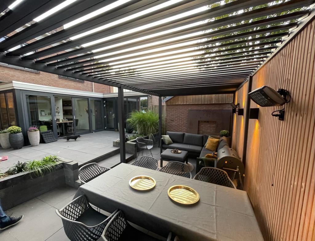 Moderne Terrasse mit Lamellenüberdachung, die teilweise Schatten spendet. Eine gemütliche Sitzecke verfügt über eine graue Couch, Stühle und einen Couchtisch. Ein Esstisch ist mit zwei goldenen Tellern gedeckt. Topfpflanzen und stimmungsvolle Beleuchtung werten den Außenbereich auf und schaffen eine perfekte Kundengeschichte.