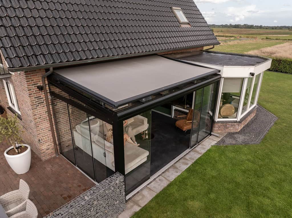Moderne Terrassenüberdachung als Wintergarten mit seitlichen Glaswänden und integrierter Beschattung, angebaut an ein Einfamilienhaus.