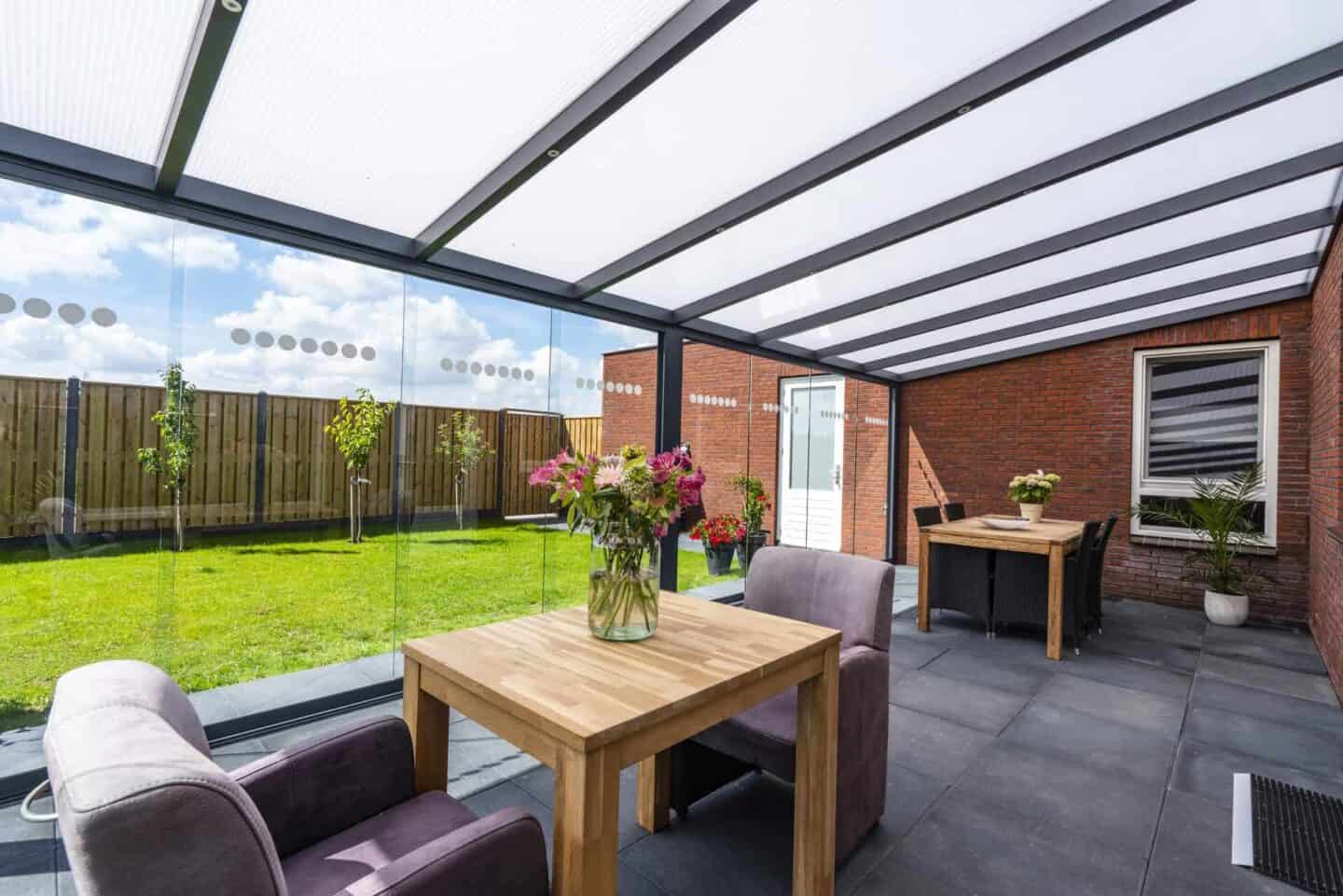 Polycarbonat-Terrassenüberdachung mit Glaswand. Sowie einer kleinen Sitzecke mit Tisch.